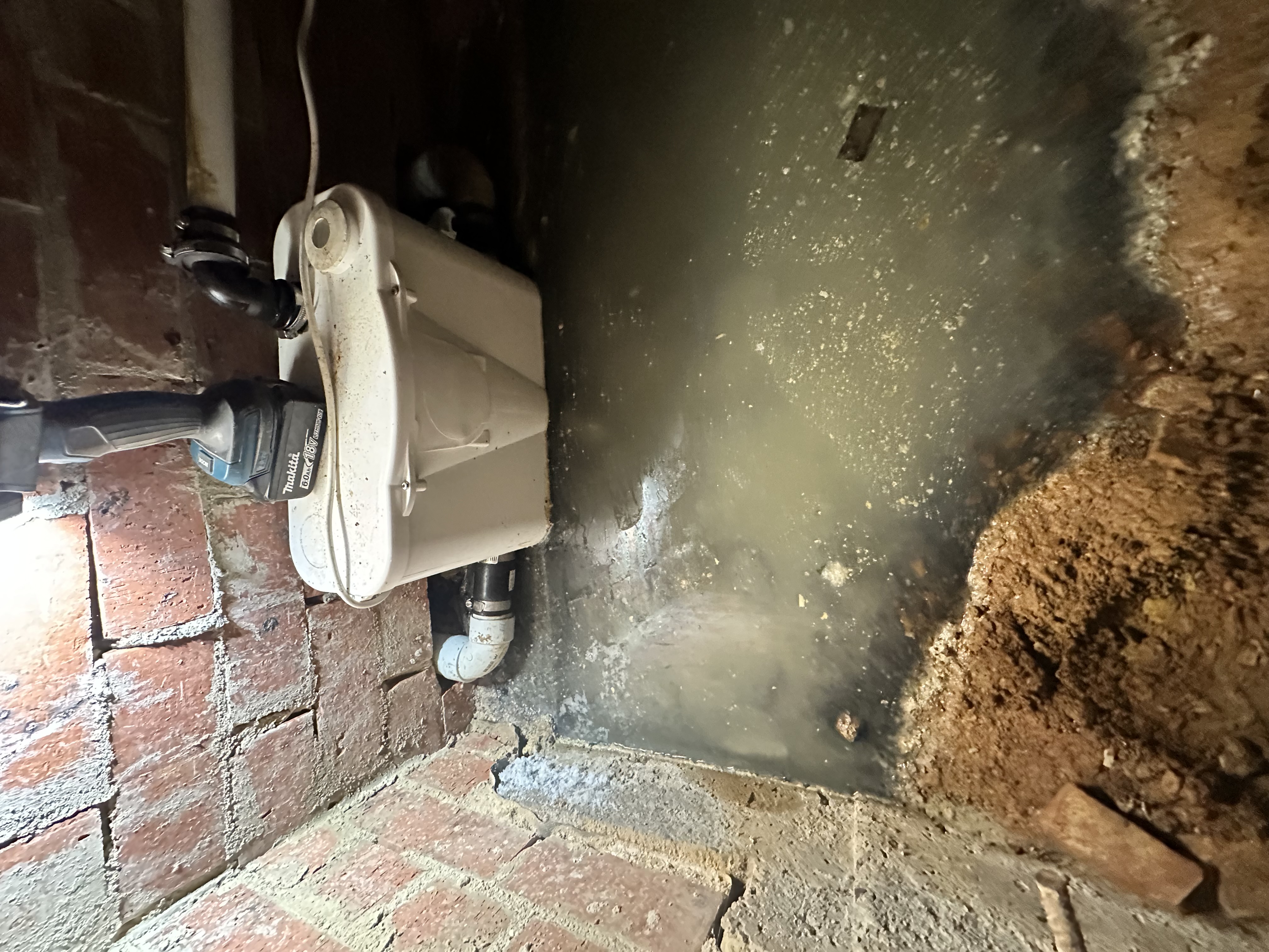 Saniflo macerator basement transfer pump retrofitted into an old red-brick subfloor on a heritage Norwood property